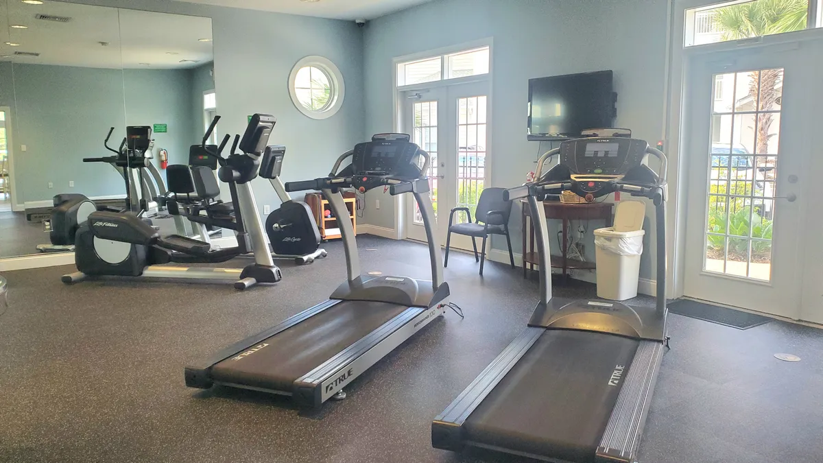 A bright, modern fitness center filled with treadmills and elliptical machines. Large windows flood the space with natural light, creating an energizing atmosphere perfect for exercise and social interaction among guests.