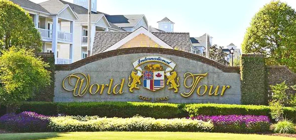 The welcoming entrance to the World Tour Golf Course, with a prominent sign, landscaped gardens, and a glimpse of the golf course beyond. The scene suggests easy access to recreation and a lush, outdoor setting.