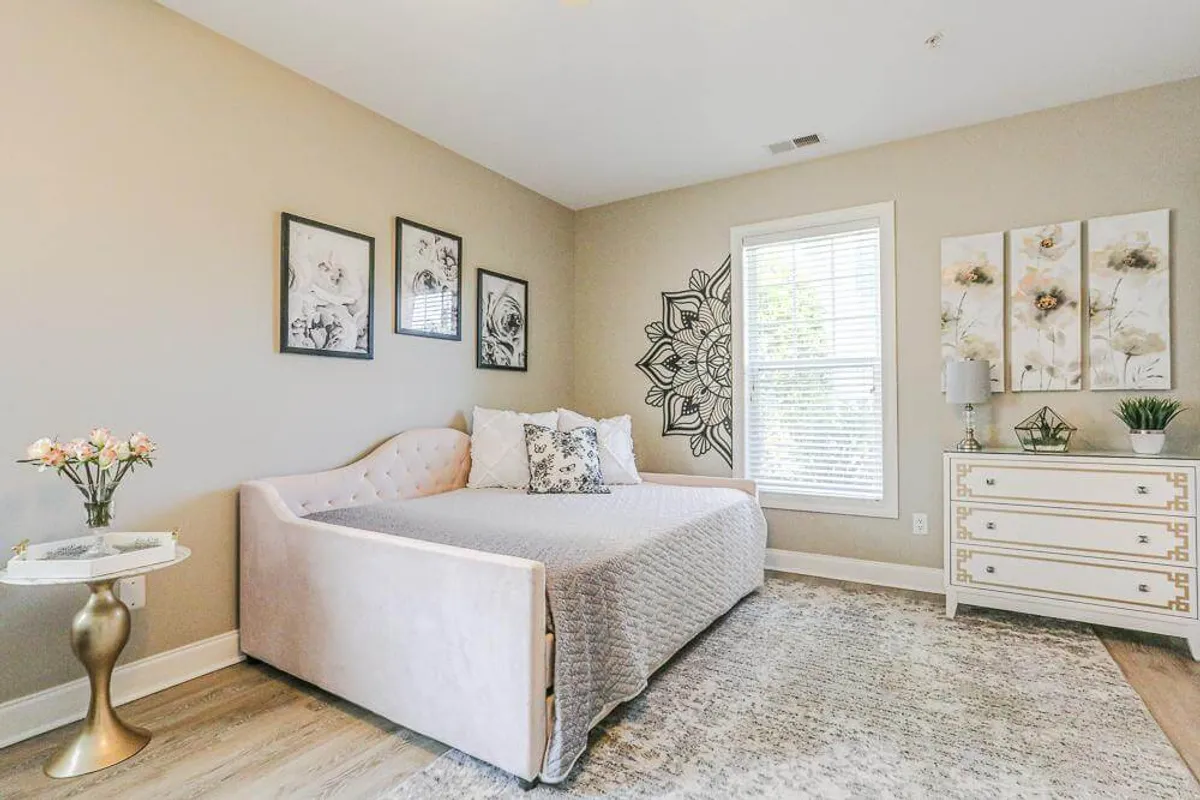 The image showcases a serene and inviting efficiency studio interior with a plush bed adorned in soft linens, tasteful wall art, a cozy nightstand, and sunlight streaming through a large window. The setup evokes a peaceful atmosphere, perfect for unwinding with a morning coffee or curling up with a good book.