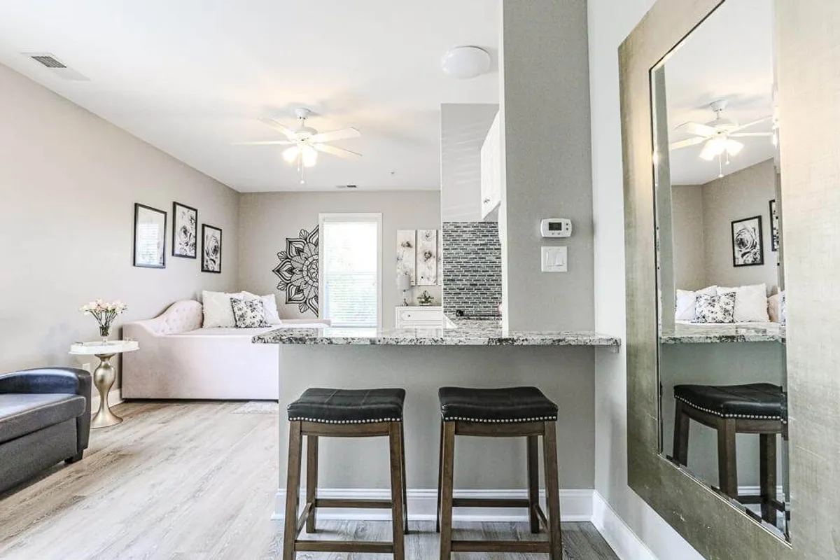 A cozy and stylish living area with a granite countertop, stylish bar stools, a decorative mirror, and a light-filled lounge space. The ambiance is welcoming, ideal for sharing intimate meals or relaxing together.